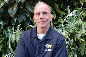 Portrait of IEEE Fellow Rory Cooper in a navy blue polo with greenery in the background