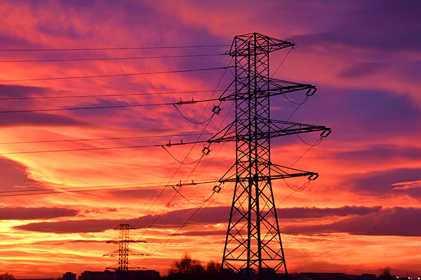 A high voltage line traction pole silhouette against a picturesque cloudy sunset in purple, red, and orange.