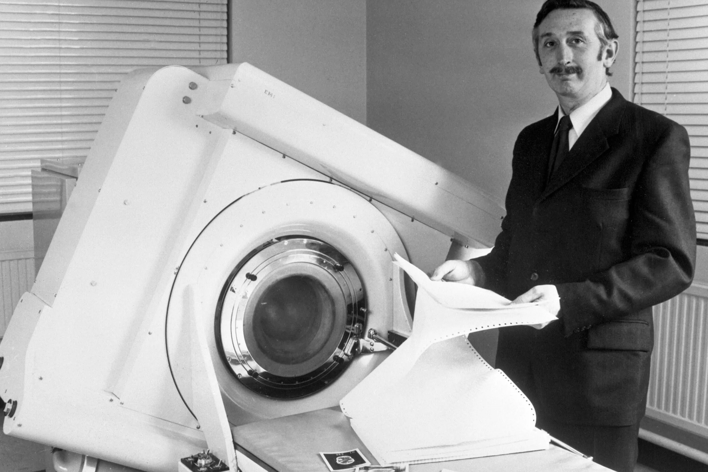 Research engineer Godfrey Hounsfield invented the CT scanner to create three-dimensional brain images. Photo of Hounsfield standing next to CT scanner.