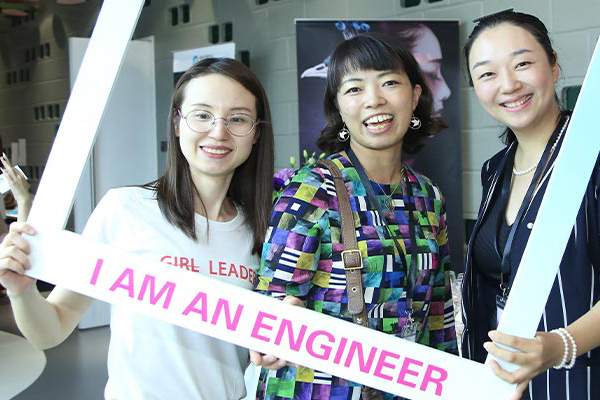 Three young women pose for a photograph, holding a frame that reads I Am an Engineer.