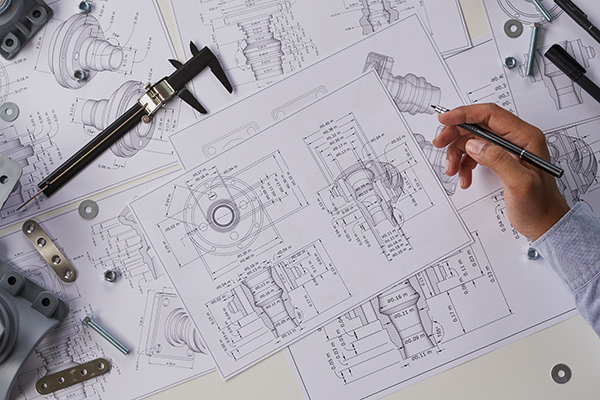 A hand holding a pen hovers over a complicated, large blueprint.