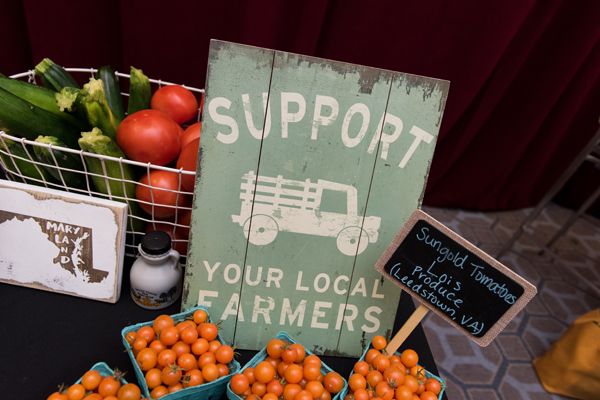 A sign reads 'Support your local farmers.' It sits on a table at a conference, along with various vegetables.